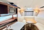 Compact yacht galley and seating area with a wooden table, white leather booth seating, and a stainless steel sink on the left; built-in microwave and storage cabinets along the wall.