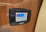 Wall-mounted digital thermostat on a wood-paneled surface; blue display shows 66 with control buttons surrounding it.