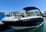 Black and white motorboat docked at a marina with its top open, hull registration CF 2364 VW visible and calm water in front of waterfront buildings.