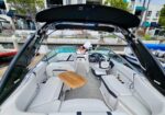 Open cockpit of a white luxury motorboat with U-shaped seating, a wooden table, helm controls, and a black canopy.