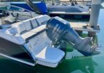 White and gray speedboat docked at a marina with a large Yamaha outboard motor tilted up on the stern and surrounding water reflections.