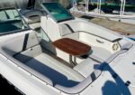 White boat cockpit with L-shaped cushioned seating and a small wooden table between the benches.
