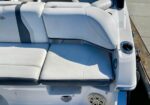 White boat seating area with cushioned benches and backrest, cup holder on the right, and a speaker grille below near the dock.