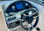 Boat helm with black and chrome steering wheel, digital display, gauges, and switch panel on a white console.