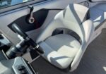 Captain's white helm seat at the boat's steering station, with a black steering wheel and throttle nearby, plus a red safety lanyard attached to the dash edge