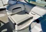 Rear seating area of a speedboat with light gray upholstery and a fold-down armrest. Two cup holders are built into the side wall. Inset storage behind the seat.