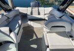 U-shaped white and gray boat seating around a deck with a sun lounge on the right; water and marina visible in the background.