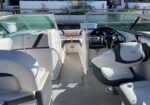 Interior of a white luxury motorboat: helm with steering wheel on the right, plush seating along both sides, and a central open walkway toward the bow.