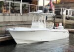 White center-console powerboat docked at a marina, tied to a concrete slip with an American flag in the background.