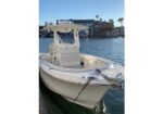 White motorboat docked at a marina with blue water and buildings in the background.