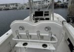Front view of a white boat cockpit at a marina, showing the helm with electronics, a curved backrest with rod holders, and two cup holders in the console.