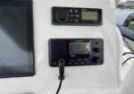 Boat helm with Garmin marine chartplotter and Fusion stereo mounted on a white console, beside a large display screen