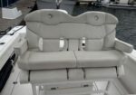 Two white cushioned boat cockpit seats with diamond stitching and armrests, mounted on a white deck near a marina.
