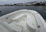 White motorboat bow with seating and storage, docked in a marina with buildings in the background.