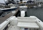White powerboat cockpit with cushioned seating and a cooler beneath the seats, docked at a marina with other boats in the background.