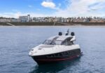 Luxury motor yacht cruising near a coastal city with high-rise buildings in the background on calm blue water