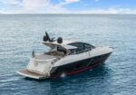 Rear view of a white luxury motor yacht cruising on calm blue water, with an open aft lounge area.