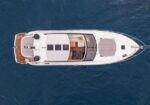 Top-down view of a white luxury motor yacht on deep blue water, showing the deck, seating area, and cockpit.
