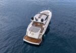 Aerial view of a white luxury motor yacht cruising on calm blue water, with teak deck and open aft seating area.