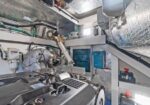 Industrial mechanical room featuring a large diesel engine with belts and hoses, silver insulated ducts, and a blue control panel on the wall.