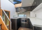 Modern yacht galley with white countertop, dark cabinets, sink, microwave, and a skylight above it.