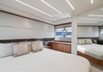 Luxurious yacht cabin with a large white bed, decorative pillows, wooden cabinets, and a round porthole window.