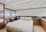 Luxury yacht cabin with a large bed, bedside tables, beige throw pillows, and a seating area by porthole windows with ocean view and wood cabinetry.
