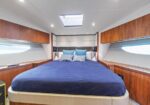 Luxurious yacht cabin with a large centered bed in blue bedding, wood paneling, and built-in storage along the sides.