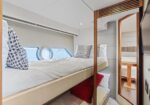 Yacht cabin with upper and lower bunks, beige mattresses, and porthole windows along the side.
