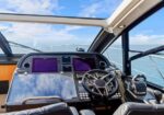 Luxury yacht cockpit with steering wheel, dual purple navigation screens, and sunroof over blue ocean horizon.