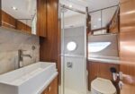 Compact yacht bathroom with wood cabinetry, rectangular white sink, chrome faucet, glass shower enclosure, porthole window, and a toilet.