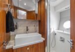 Compact bathroom with a white vessel sink on marble counter, mirrored cabinet, and a glass-enclosed shower with a circular window.