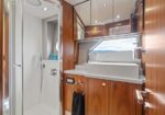 Compact yacht bathroom with white shower stall on the left and a wood-paneled vanity with a rectangular sink and mirrored cabinets on top.