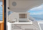 Built-in outdoor grill on a boat deck with the lid open, next to a sink and storage cabinets, sea and blue sky visible in the background.