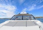 Front deck of a white luxury motor yacht with sunpads, on calm blue water under a clear sky; a small flag is visible on the windshield.