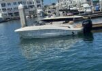 White speedboat docked at a marina with calm blue water and other boats in the background.