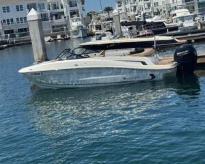 White speedboat docked at a marina with calm blue water and other boats in the background.