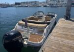 White motorboat docked at a wooden pier with beige seats and a Mercury outboard engine, calm marina in the background.