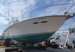 White motorboat on a cradle in a shipyard, raised for maintenance against a blue sky.