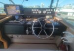 Boat cockpit with stainless steering wheel, gauge panel, GPS display, and marina visible through windshield at dockside cove.