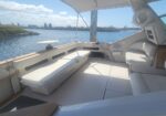 Luxurious white yacht interior with cushioned benches and cockpit visible to the right, overlooking calm water and shore.