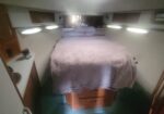 Narrow boat cabin with a centered bed, lavender bedding, and wooden drawers beneath the mattress.