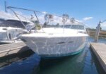 White motor yacht docked at a marina on a sunny day with blue sky and calm water.
