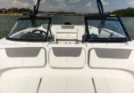 White luxury speedboat interior with cushioned seating and grey accents, two windshields, on a calm lake with shoreline in background