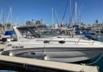 White motorboat named 'Two Best Days' docked at a marina, with sailboats and a clear blue sky in the background.