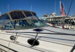 White motor yacht docked at a marina on a sunny day, with an American flag visible in the background.
