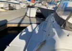 White motorboat docked at a marina, with a wooden pier and other boats in the background; shadow on deck nearby.