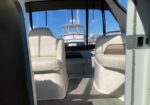 Interior of a boat cabin with two white cushioned seats and a view of a marina through the windshield.