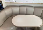 Beige curved booth seating around an oval beige table in a compact dining nook, with storage cabinets above.