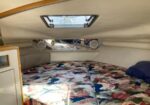 Small boat cabin with a floral bedspread and a rectangular hatch above the sleeping area, framed by curved wood trim.